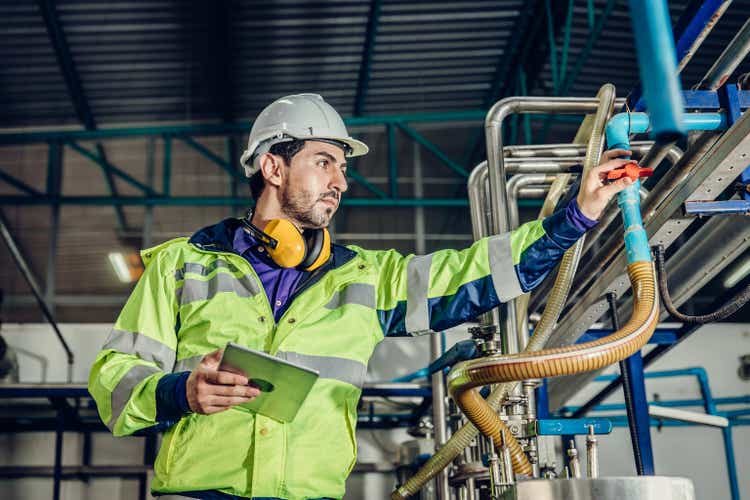 Young hispanic latin engineer working in a heavy industrial factory. worker control oil gas water pipe in plant.