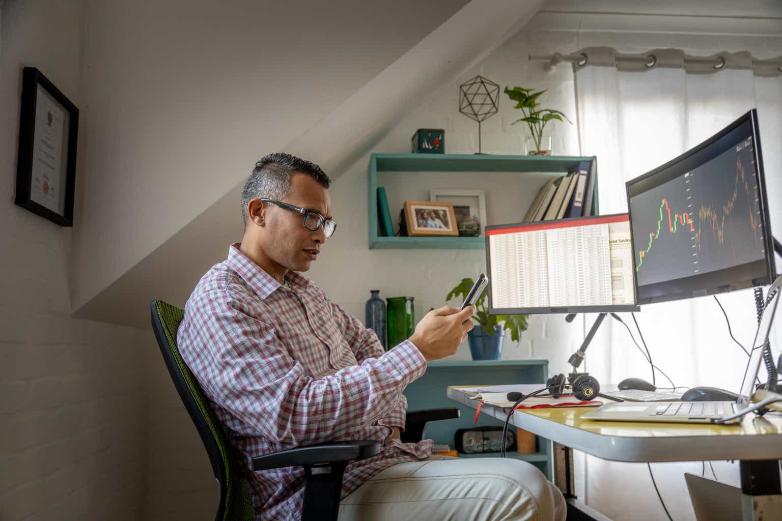 Man looking at currency trading app on his smart phone from his home office