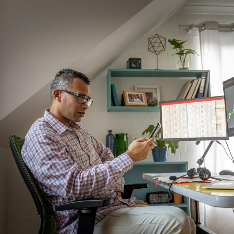 Man looking at currency trading app on his smart phone from his home office