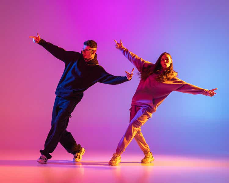 Two young people, guy and girl in casual clothes dancing contemporary dance, hip-hop over pink background in neon light.