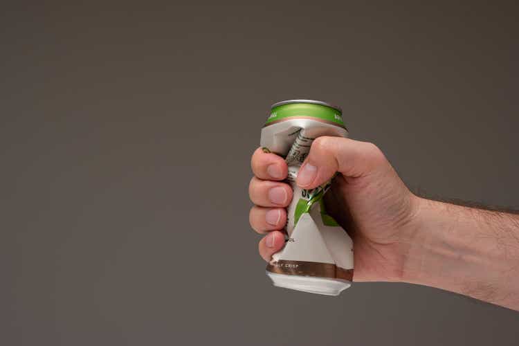 Caucasian male holding a crushed tin metal beer can. Close up studio shot, isolated on brown background