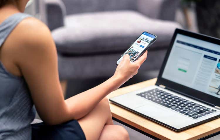 Social media profile page in smartphone screen at work. Woman looking at feed, status update or post with mobile phone. Inefficient lazy worker avoiding job.