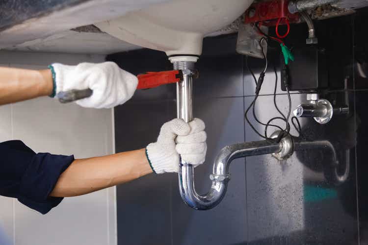 Plumber fixing white sink pipe with adjustable wrench.