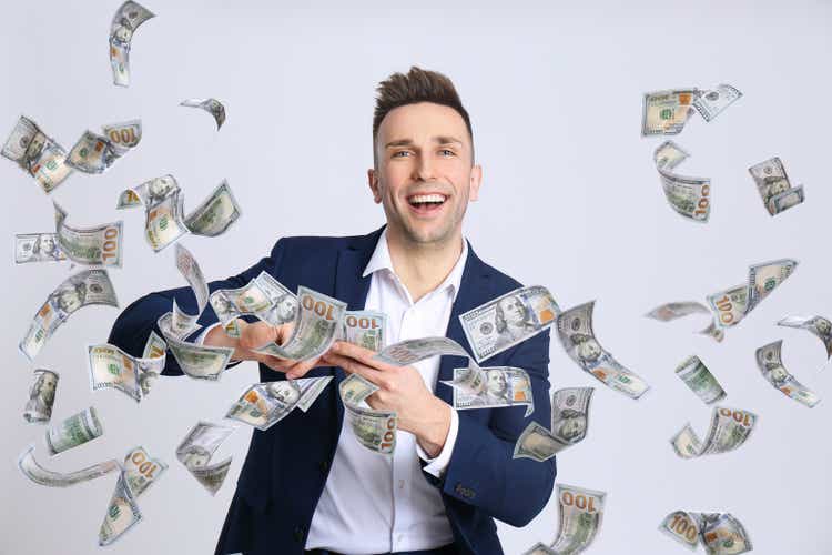 Happy young man with money on light background