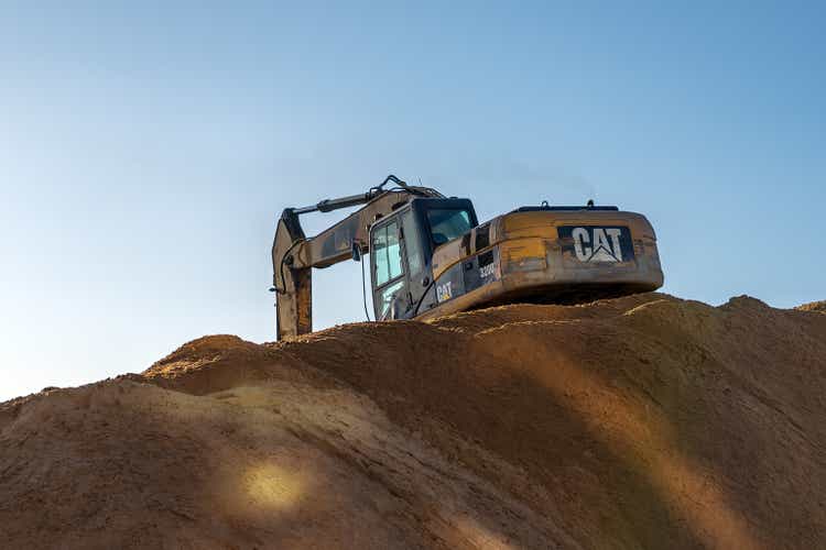 Yellow excavator 3/4 back view digging at the top of a pile of sand.