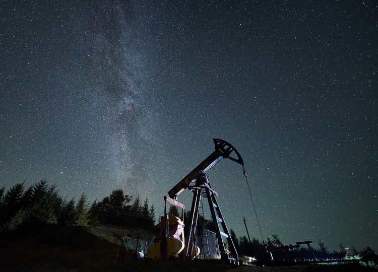 Oil pump jack at night time under starry sky.