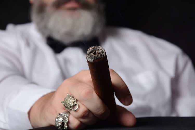 Elegant man wearing white shirt holds a smoking Cuban cigar
