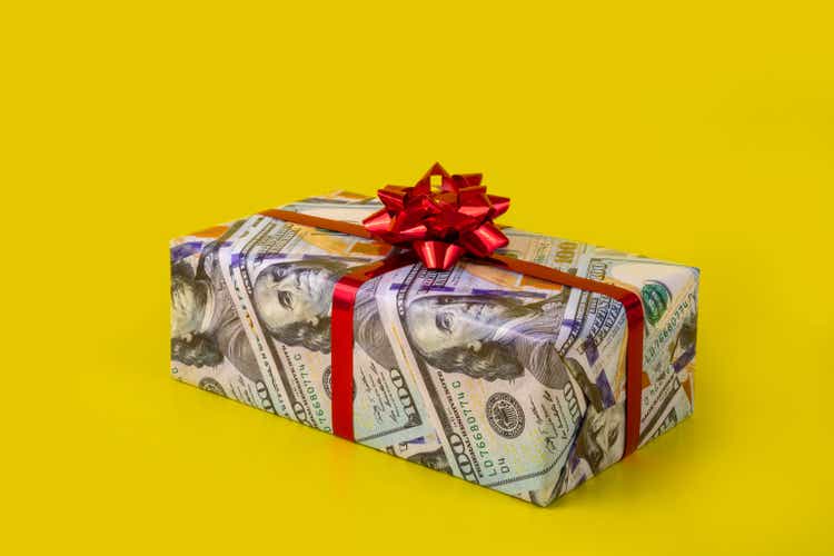 Isolated gift box wrapped in wrapping paper with 100 dollar bill picture on yellow background