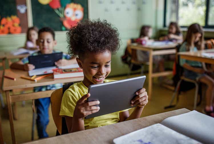 Happy black elementary school student using touchpad in a class.