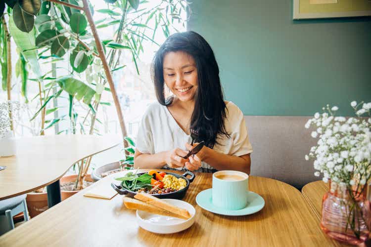 Young Asian woman sits at table and eats in vegan cafe