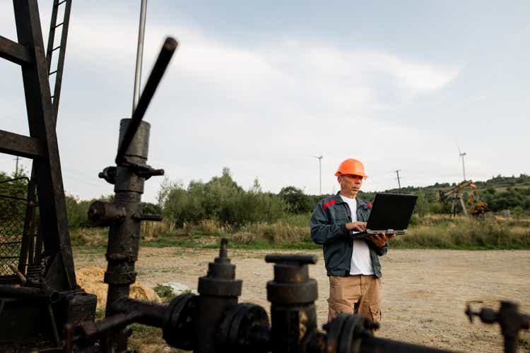 Oil worker engineer using laptop near oil pumpjack on the oil field