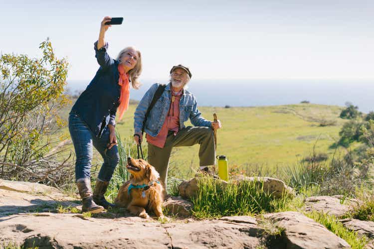 Senior couple taking selfie with dog during hike on sunny day