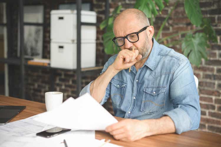 mature adult man working from office ( with laptop, paperwork, Negative Emotion)