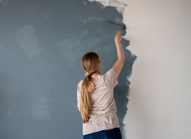Woman painting a wall of her new house with a blue or grey color