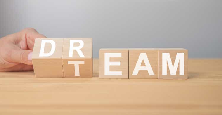 Dream team. Businessman turns cubes and changes the word dream to team. Wooden table, grey background. Business and dream team concept, copy space.
