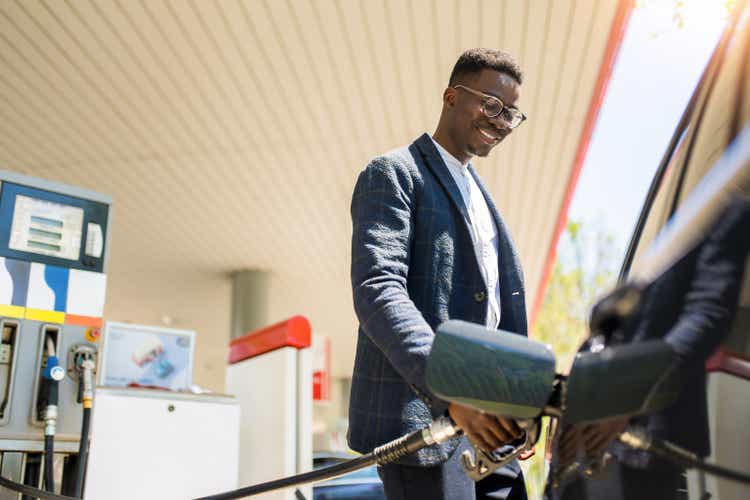 Happy young African American man refueling his car the gas station.