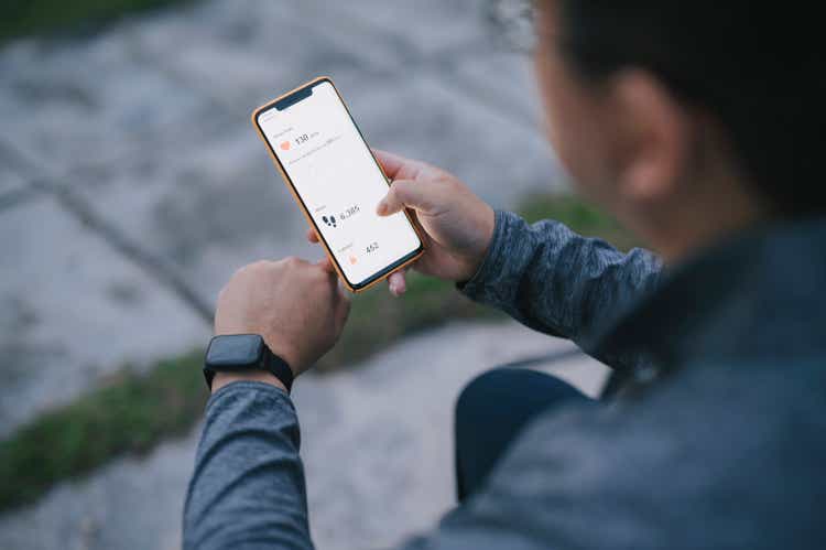 Over shoulder view asian chinese man using fitness tracker mobile app connecting to fitness tracker at public park after exercise in the morning