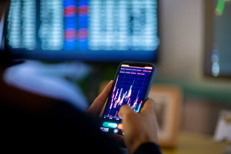 Man looking at forex trading app on his smart phone at his home office