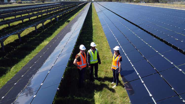 Multiracial Group Of Three Engineers Surrounded By Solar Panels