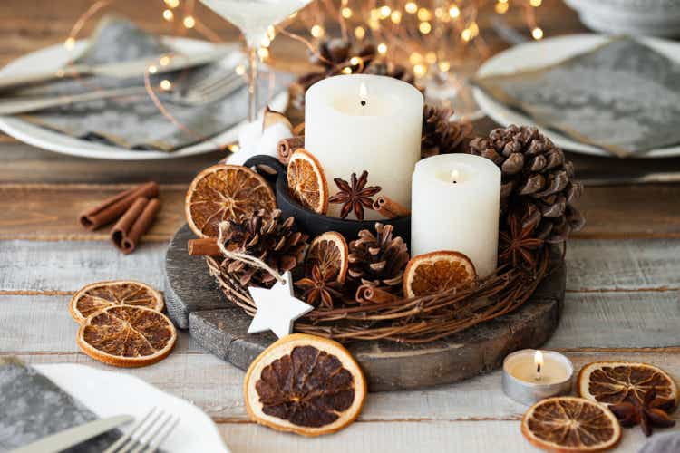 Rustic decor for christmas holiday family dinner. Center piece with white candle, dry orange, cones, cotton. Zero waste eco friendly home decoration. Cozy atmosphere, wooden background. Close up