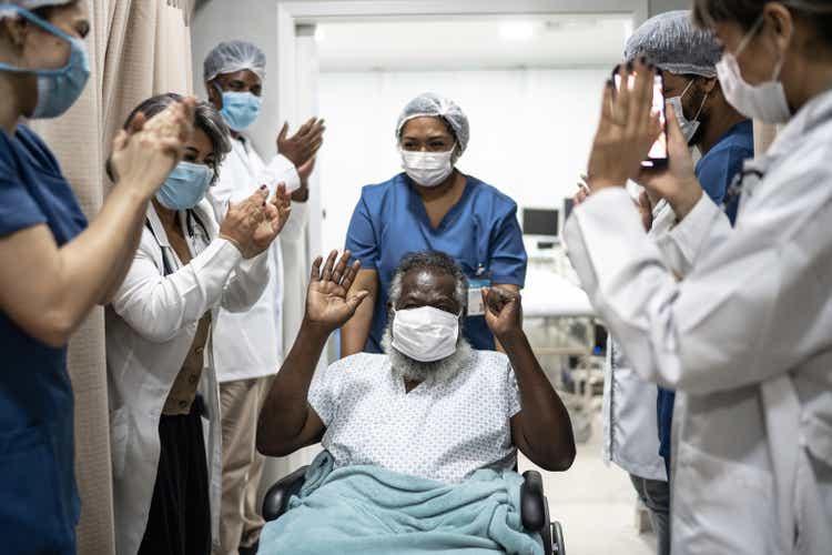Врачи и медсестры празднуют выход пожилого человека из больницы после выздоровления - в защитной маске для лица