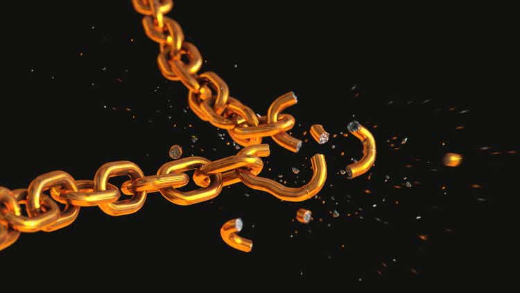 Close-up side view on a shiny gold-colored chain in the process of breaking into many scattered pieces, isolated on a black background.