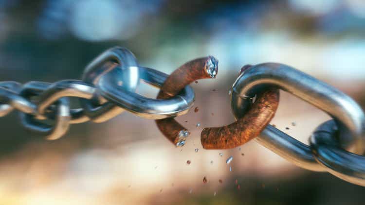 Dramatic close-up on a breaking chain with a rusty link and fragments flying off in blurred motion, on a defocused multi-colored background.