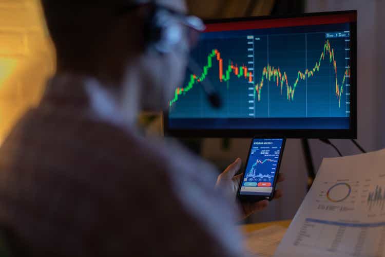 Man looking at currency trading app on his smart phone from his home office