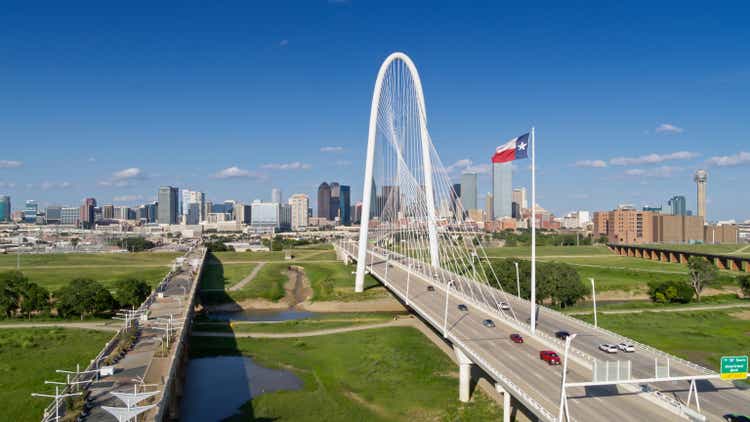 Drone Shot of Texas State Flag Waving Over Margaret Hunt Hill Bridge with Dallas Skyline Beyond