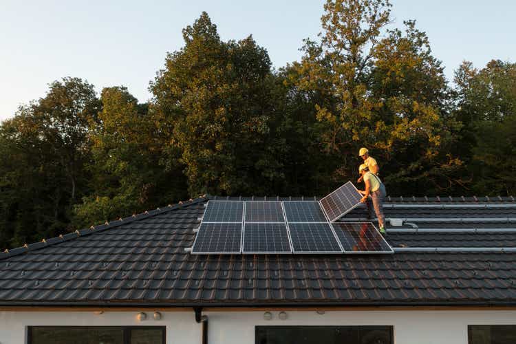 Two Workers Installing Solar Panels On Modern House.