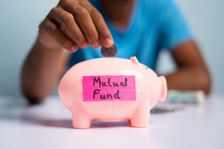 Concept of mutual fund investment, showing with hands placing coins inside the piggy bank with mutual fund sticker