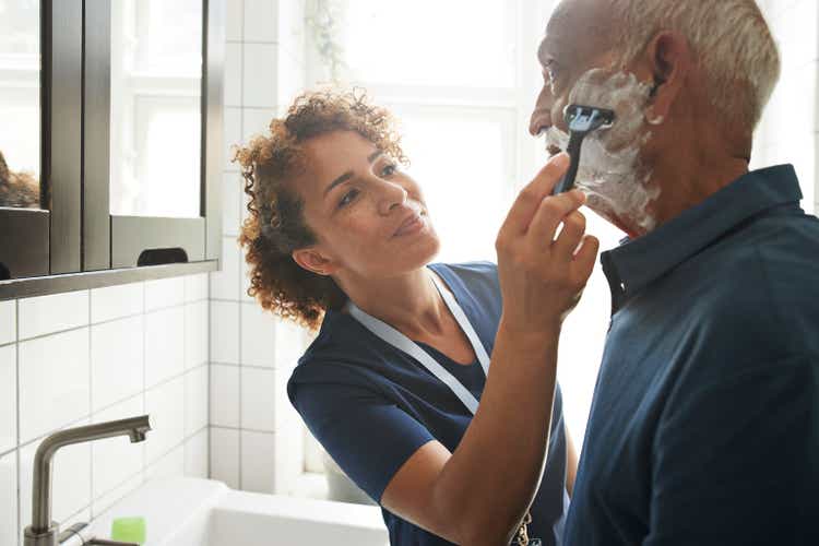 Healthcare worker assisting senior man in shaving