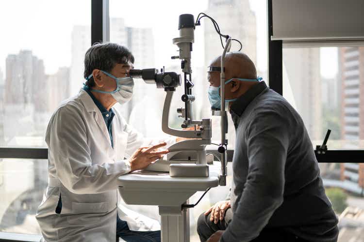 Optometrist examining patient"s eyes - wearing face mask
