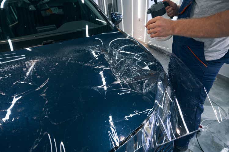 Car service specialist spraying water on protective paint film on hood