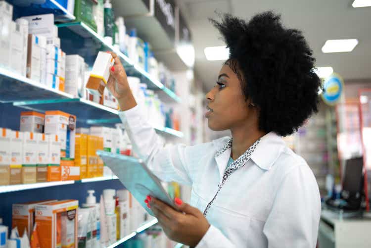 Young pharmacist checking shelves with digital tablet in pharmacy
