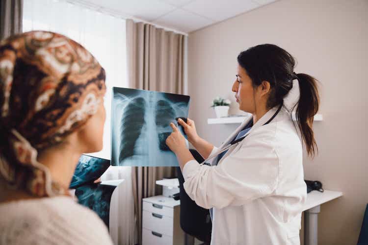 Hispanic female expertise giving advice to cancer patient while examining x-ray at doctor"s office