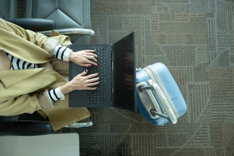 Close-up shot of unrecognizable woman working with laptop at airport next to luggage