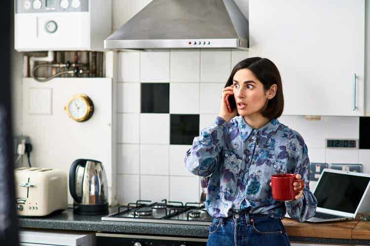 Shocked looking woman on phone in kitchen