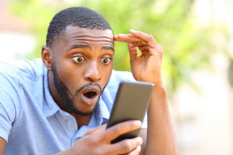 Amazed black man checking smart phone in a park