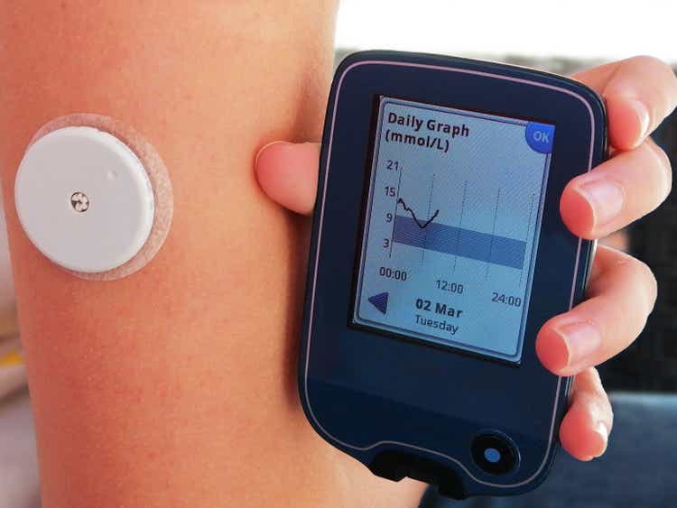 Reading a glucose with device for continuous glucose monitoring in blood – CGM. On arm is placed white sensor witch send information to the CGM device. Daily graph on screen