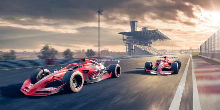 Two Red Racing Cars Moving At High Speed Along Racetrack At Sunset