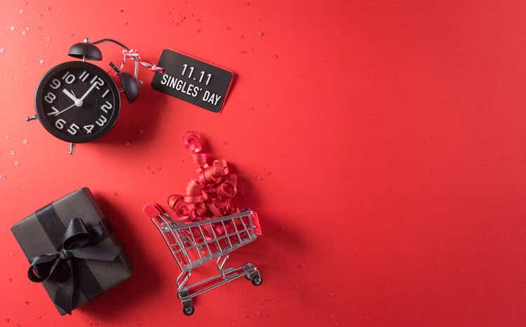 Online shopping of China, 11.11 singles day sale concept. Top view of shopping cart, black christmas gift boxes with sale card on red background with copy space.