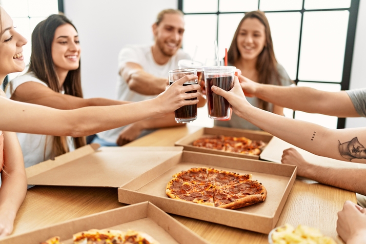 Group of young friends smiling happy eating italian pizza and toasting with cola beverage at home.