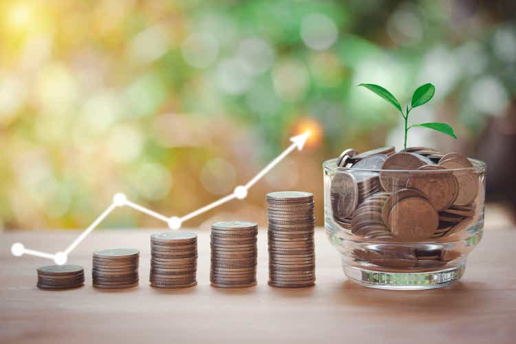 A glass jar with full coins and plant on top, money stacking for saving money concept, home, loan, step to keep money, big thinking on bokeh background.