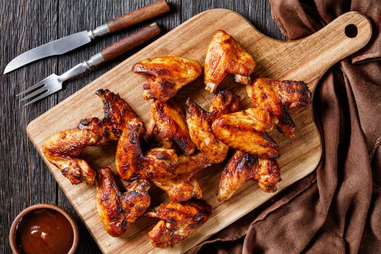 crispy fried chicken wings served on a wooden board with barbeque sauce on dark wooden table, flat lay