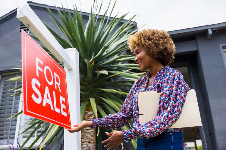 Mature real estate agent adjusting for sale sign in front of home