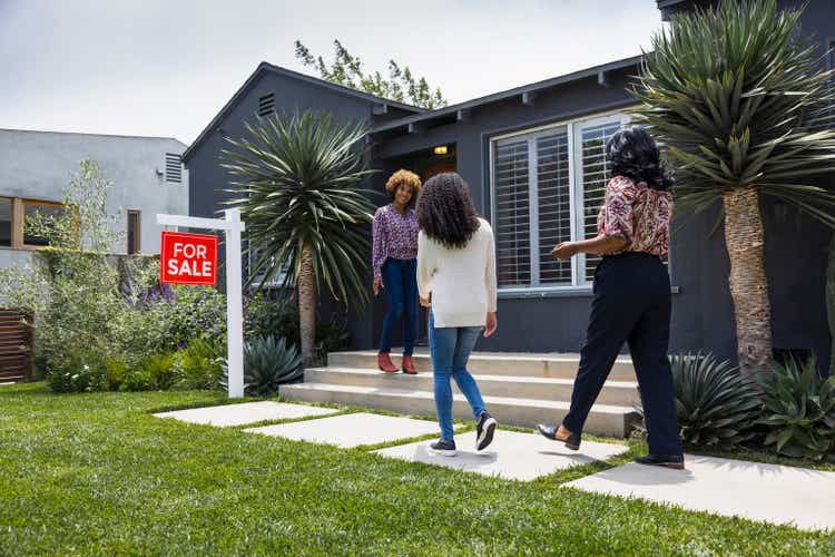 Full length of saleswoman greeting female customers while standing outside house