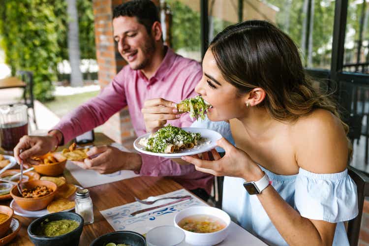 joven latina comiendo tacos mexicanos en la terraza de un restaurante en México Latinoamérica, sintiéndose feliz en un día de verano