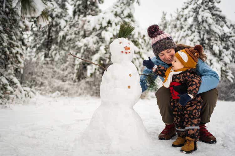 Playful toddler boy, helping his mom to make a snowman