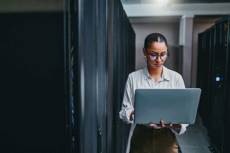 Shot of a young woman using a laptop while working in a server room